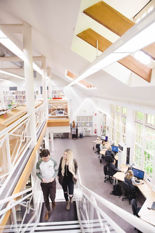 Two students ascend a staircase in a brightly lit and open plan university library.